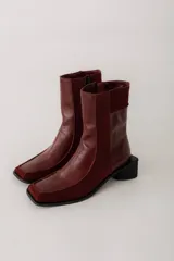 Bota corta de cuero color bordó, con punta cuadrada y taco bloque bajo. Cierre lateral con cremallera.
