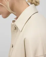 Bomber color beige de piel sintética con cuello solapa, manga larga redondeada con pinza en el codo, cierre frontal con botones y bolsillos laterales.