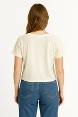 Remera crudo/natural de algodón con cuello redondo y detalle de encaje en el pecho. Tiene un nudo en la parte delantera.