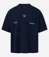 Remera de algodón azul marino, corte oversized, con cuello redondo y mangas cortas. Presenta un pequeño estampado en el pecho con texto y un logo circular, y un estampado más grande con el texto "Broad Plans" en la parte inferior derecha del frente.