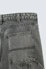 Pantalón gris de corte relaxed fit, con cinco bolsillos, efecto lavado, aplicación de tira y bolsillo multifunción en perneras. Cierre frontal con cremallera y botón.