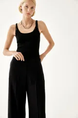 Pantalón negro de corte ancho y tiro alto, con elástico en la parte posterior de la cintura, cierre oculto con corchete en un lado, bolsillos laterales discretos y pliegues adelante y atrás.