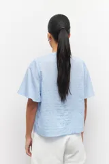 Blusa celeste a rayas verticales con cuello mao, mangas cortas y lazo en el frente.