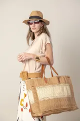 Bolso tipo shopper de rafia en tonos beige y camel, con cierre superior y asas de cuero para llevar al hombro.