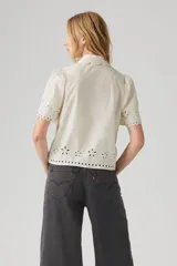 Camisa color crema con bordado calado, cuello clásico, manga corta abullonada y cierre frontal con botones.