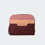 Billetera Rip Curl con diseño color block, combinando secciones en color bordó, beige claro y rosa pálido. Presenta el logo Rip Curl grabado en la sección central beige. Tiene cierre de cremallera lateral.