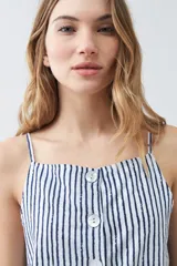 Chaleco con estampado a rayas verticales azules y blancas, con breteles finos y cierre frontal con botones. Presenta dos bolsillos frontales a la altura del pecho.