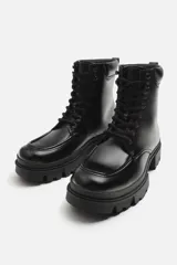 Bota negra de cuero con cordones, suela track y tirador trasero.