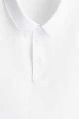 Remera polo blanca de manga corta en piqué liviano de mezcla de algodón con cuello y tapeta de botones. Corte ajustado que realza el contorno del cuerpo creando una silueta entallada. Confeccionada con tejido funcional COOLMAX®, una fibra exclusiva de poliéster de secado rápido que elimina la humedad y regula la temperatura corporal proporcionando un ajuste cómodo y suave.