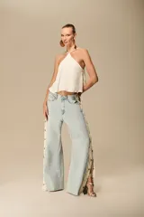 Pantalón de jean de lavado claro, corte recto y tiro medio, con paneles laterales de encaje blanco con botones a presión visibles a lo largo de las costuras laterales.