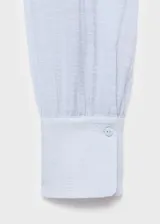 Blusa de manga larga color celeste claro con textura sutil, cuello alto con lazo largo incorporado que cae al frente.