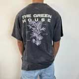 Remera negra con efecto gastado y estampado en la espalda con la frase "The Green House" y un diseño de hojas en color lila.