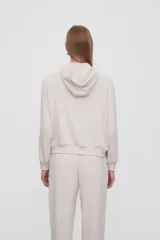 Campera con capucha color beige claro con cierre frontal y bolsillos laterales. Presenta una banda blanca en las mangas. Corte holgado.