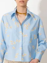 Camisa celeste con estampado floral, confeccionada en poplin con acabado paper touch, acceso mediante cartera oculta con botones y dos bolsillos plaque en el frente.