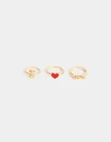 Set de tres anillos dorados de metal con diferentes dijes: un oso, un corazón rojo y la palabra 'Love'.