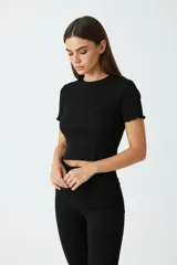 Remera negra de punto canalé con cuello redondo y mangas cortas con terminación ondulada. Presenta un aplique bordado con forma de moño en el frente.