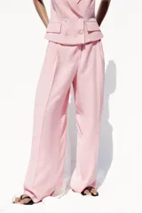 Pantalón ancho color rosa claro, de tiro alto con pinzas delanteras, bolsillos frontales y cierre frontal con cremallera y botones.