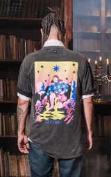 Remera negra con efecto nevado, de manga corta y cuello redondo, con calce oversize. Presenta una estampa en la espalda inspirada en el arcano "La Estrella" del Tarot, con una figura femenina vertiendo agua de dos cántaros, rodeada de estrellas y vegetación en colores vibrantes como amarillo, azul, rosa y verde.