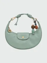 Bolso hobo de cuero color marrón, con cierre de solapa con botón a presión y correa corta para llevar al hombro. Incluye charm colgante con cuentas de madera y piedra.