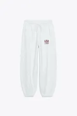 Pantalón jogger gris melange de tiro alto con cintura elástica ajustable y cordón. Tiene bolsillos delanteros y puños elásticos en los tobillos. Estampado con la leyenda "USA 1989" en color bordó.