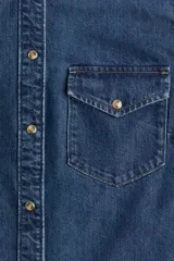 Camisa de denim azul con cuello clásico, cierre frontal con botones a presión, dos bolsillos con solapa abotonada en el pecho, mangas largas con puños abotonados y canesú en la espalda.
