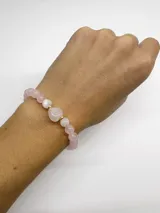 Pulsera elástica con cuentas de cuarzo rosa y piedra luna de 6mm, cuenta central en forma de corazón y dije de perla de río. Terminaciones en acero con baño dorado.