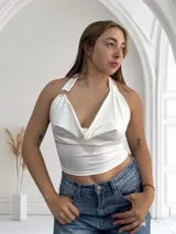 Top blanco con escote drapeado, corte cropped y espalda descubierta. El cuello halter se ata con un aro metálico.