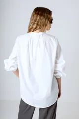 Camisa blanca de corte holgado, cuello mao y mangas largas con puños fruncidos.
