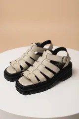 Sandalias de tiras anchas color blanco, con plataforma track negra y hebilla lateral ajustable.