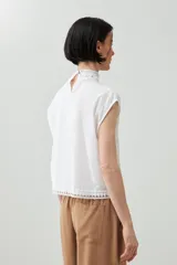 Blusa blanca sin mangas con cuello alto y detalles de puntilla.