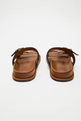 Sandalias planas negras con dos tiras anchas y hebillas doradas.
