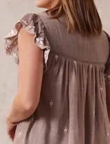 Blusa color marrón claro de algodón con bordados y calados blancos. Tiene cuello a la base, escote en V con lazo de ajuste y mangas cortas amplias.