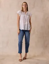 Blusa color marrón claro de algodón con bordados y calados blancos. Tiene cuello a la base, escote en V con lazo de ajuste y mangas cortas amplias.