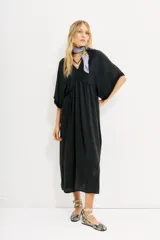Vestido midi negro de calce amplio y mangas al codo. Tiene apliques de gasa en escote y mangas, y recortes con frunce en la cintura.