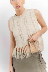 Chaleco de hilo color crema, con cuello redondo y diseño calado. Presenta flecos en el ruedo.