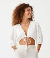 Blusa cropped blanca de laise texturizado con mangas 3/4 ajustadas y lazo en el bajo.
