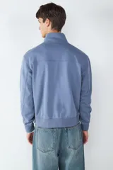 Buzo celeste de corte relajado con media cremallera frontal y cuello subido. Confeccionado en tejido suave con acabado efecto lavado. Puños acanalados y bajo elástico para un mejor ajuste.