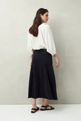 Falda midi de denim negro con tiro bajo, corte evasé, costuras verticales y ruedo desflecado.