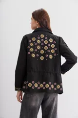 Campera negra de algodón con bordados de flores y lentejuelas. Tiene corte recto, ajuste interno en la cintura, bolsillos con solapa y cierre frontal.