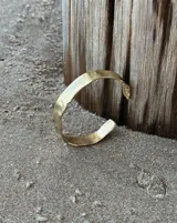 Pulsera tipo esclava abierta, con acabado rústico y textura irregular, en tono plateado. Se vende por unidad.