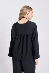 Blusa negra de manga larga con cuello en V y cierre con botones.