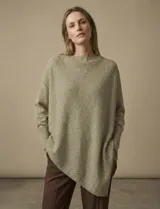 Poncho de tejido lurex color verde oliva con brillo sutil, de corte amplio y manga larga con puños acanalados. Presenta un bajo asimétrico con caída diagonal.