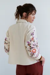 Chaqueta color crudo con bordados de flores azules y naranjas.
