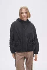 Campera negra de manga larga con capucha, cierre frontal con botones a presión, bolsillos laterales y cordón ajustable en la cintura.