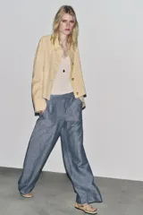 Pantalón de tiro bajo color azul con textura de lino, de pierna ancha, con bolsillos delanteros y traseros. Cierre frontal con cremallera, botón y ganchos metálicos.