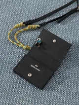 Tarjetero negro de cuero vacuno con broche imán y forrería de tejido jacquard. Incluye divisiones internas y correa combinada de cuero y cordón para colgar al hombro. Aplique Groovy en el frente.