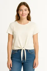 Remera crudo/natural de algodón con cuello redondo y detalle de encaje en el pecho. Tiene un nudo en la parte delantera.