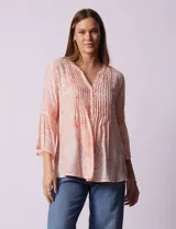 Blusa de gasa estampada color salmón con flores blancas, marca Ruby Rd. Cuello a la base, escote en V y abertura central con botones. Delantera con plisados. Largo de manga ¾ con terminación amplia.