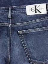 Pantalón de jean azul oscuro, de corte slim y talle alto, con diseño de cinco bolsillos y cierre con cremallera y botón.