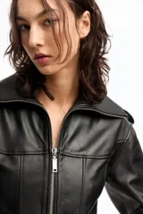 Campera corta de cuero ovino italiano color negro, con silueta tipo corsetera, cierre metálico frontal, mangas anchas fruncidas y forro de acetato con logo Ginebra.